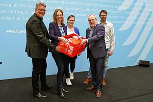 Wolfgang Klose, Pia Stapel, Dr. Martin Schölkopf, Anne Eckert und Jonas Vorderwülbecke halten gemeinsam eine rote Kiste, in der zahlreiche Briefe liegen. 