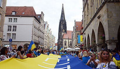 Eine riesige Ukraine-Fahne mit dem Wort „Freiheit“ zierte während der Kundgebung den Prinzipalmarkt in Münster. Im Hintergrund sieht man den Turm der St.-Lamberti-Kirche.