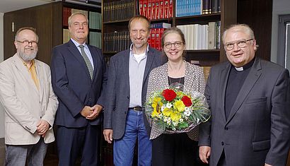Vier Männer und eine Frau, die einen Blumenstrauß hält, stehen in einer Bibliothek.