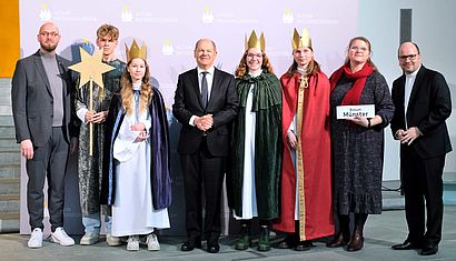 Vier als Sternsinger verkleidete Jugendliche sowie weitere Erwachsene stehen zu einem Gruppenfoto mit Bundeskanzler Scholz zusammen.