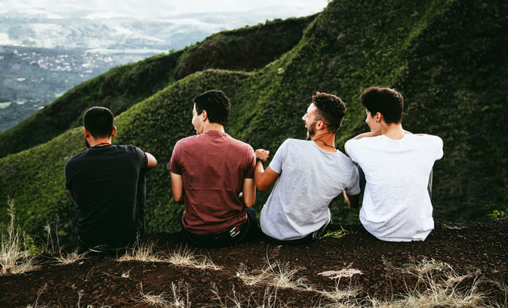 Vier junge Männer sitzen an einem Felsvorsprung und schauen ins Tal.