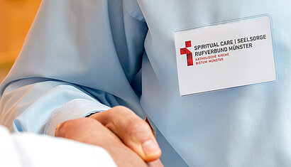 Auf dem Bild ist ein Namensschild zu sehen, dass den Schriftzug "Spiritual Care / Seelsorge: Rufverbund Münster"