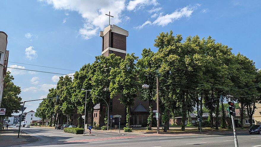 Außenansicht einer Kirche mit davor wachsenden Bäumen.