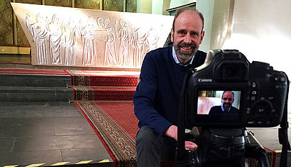 Walter Tacke sitzt auf den Stufen vor dem Altar und wird gefilmt. 