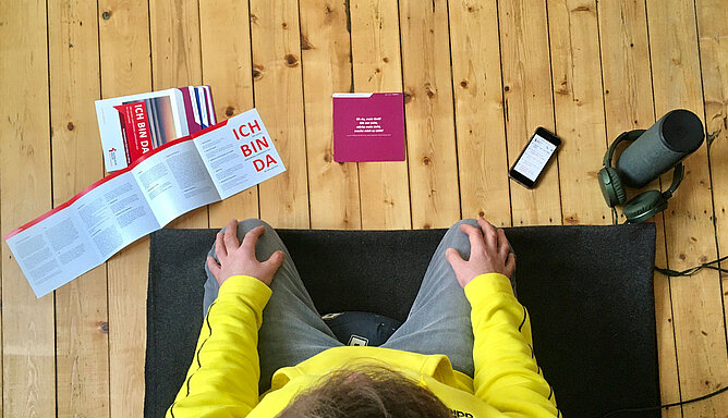 Ein Mann kniet auf einer Meditationsmatte. Er hat Impulskarten und einen Kopfhörer vor sich liegen.