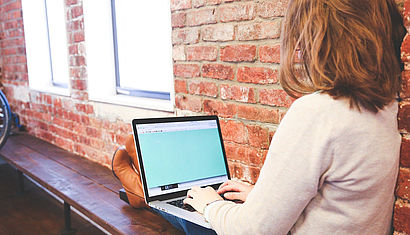 Eine junge Frau auf einer Bank arbeitet an einem Computer