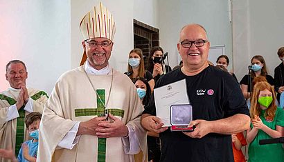 Weihbischof Lohmann steht neben Stephan Billen, der eine Urkunde und eine Schatulle in der Hand hält.