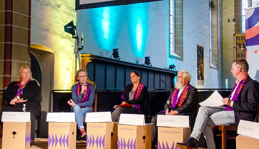 Mehrere Menschen sitzen bei einer Podiumsdiskussion und sind im Gespräch.