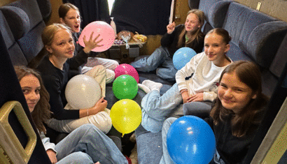 Eine Gruppe Schülerinnen sitzt in einem Zugabteil und hält Luftballons in den Händen.