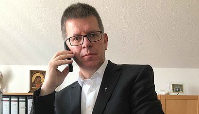 Porpst Johannes Mecking sitzt an seinem Schreibtisch und hält mit der rechten Hand einen Telefonhörer ans Ohr.