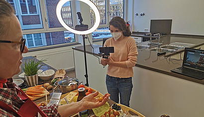 Eine Frau filmt einen Mann beim Kochen.