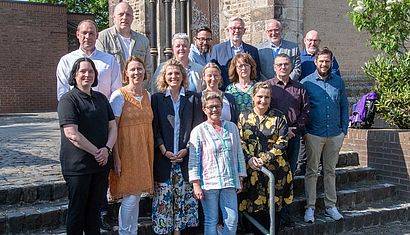 15 Frauen und Männer stehen zum Gruppenbild auf einer Treppe.