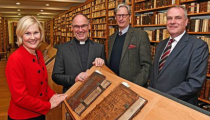 Elisabeth Maas, Weihbischof Rolf Lohmann, Wolfgang-Albert Herzog von Urach und Holger Wefers stehen an einem Lesepult in der Stiftsbibliothek.