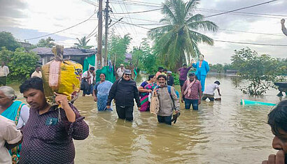 Menschen stehen kniehoch in Wassermassen, die durch die Straßen ziehen.