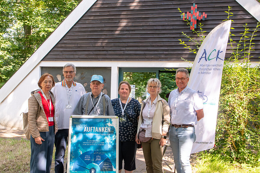Sechs Ehrenamtliche der ACK Münster stehen um einen Aufsteller herum vor der Autobahnkapelle Roxel. Sechs Ehrenamtliche der ACK Münster stehen um einen Aufsteller herum vor der Autobahnkapelle Roxel.