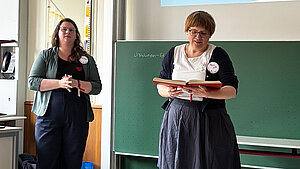 Zwei Frauen stehen erklärend vor einer Schultafel.