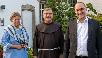 Eine Frau und zwei Männer stehen vor einem Haus.