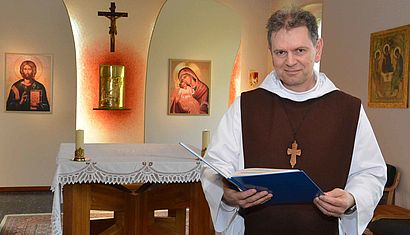Pater Markus Vogt steht in der Kapelle und hält das Fürbitt-Buch aufgeschlagen in der rechten Hand.