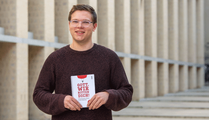 Ein Junger Mann hält ein Buch in den Händen.