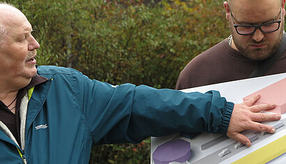 Ein Mann erklärt etwas und zeigt dabei auf einen 3D-Lageplan der Gedenkstätte Grafeneck. 