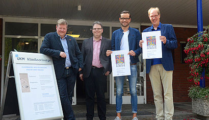 Die Initiatoren der Kunstinstallation stehen vor der Klinikkirche und halten Plakate in den Händen.