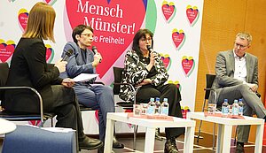 Vier Frauen und Männer sitzen auf einem Podium. Eine Frau spricht in ein Mikrofon. Vier Frauen und Männer sitzen auf einem Podium. Eine Frau spricht in ein Mikrofon.