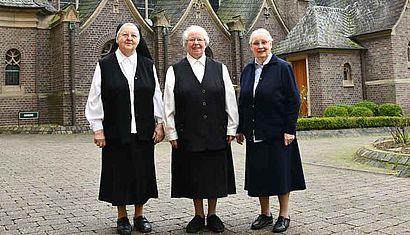 Drei Ordensschwestern stehen vor einer Kirche.