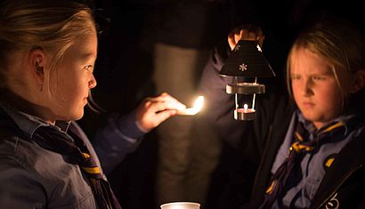 Ein Mädchen zündet mit seiner Kerze die Kerze eines anderen Mädchens an.