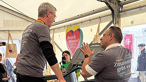 Ein Mann in grauem T-Shirt steht links auf einem Laufband. Rechts von ihm steht ein Mann und erklärt ihm dessen Handhabung. Ein Mann in grauem T-Shirt steht links auf einem Laufband. Rechts von ihm steht ein Mann und erklärt ihm dessen Handhabung.