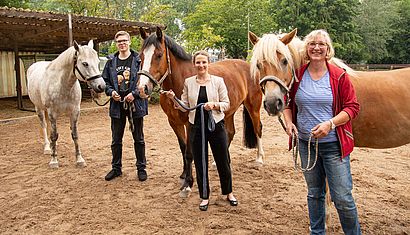 Zwei Frauen und ein Mann stehen auf einer Koppel und halten je ein Pferd.