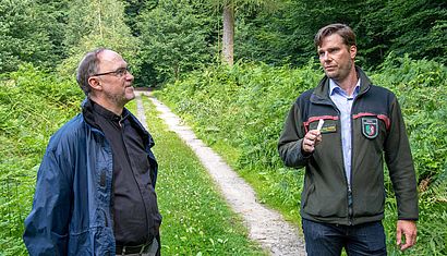 Zwei Männer stehen auf einem Waldweg und unterhalten sich.