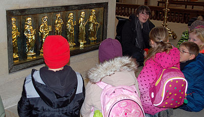 Referentin Lena Treese betrachtet mit den Kommunionkindern die goldenen Apostelfiguren.