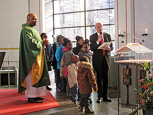 Franz-Thomas Sonka steht am Ambo, neben ihm einige Kinder und Pfarrer Frankline Anyanwu, bei seiner Einführung 2019 als Leiter der afrikanischen Gemeinde.