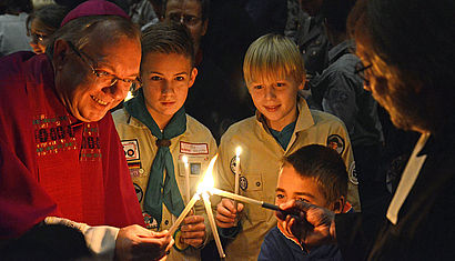 Weihbischof Hegge und Pfadfinder entzünden ihre Kerzen mit dem Friedenslicht aus Betlehem.