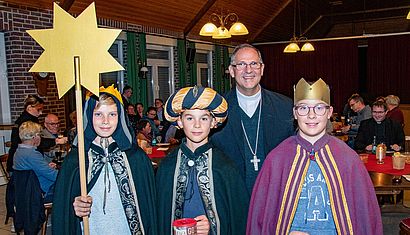 Drei als Sternsinger verkleidete Jugendliche stehen vor einem Mann.