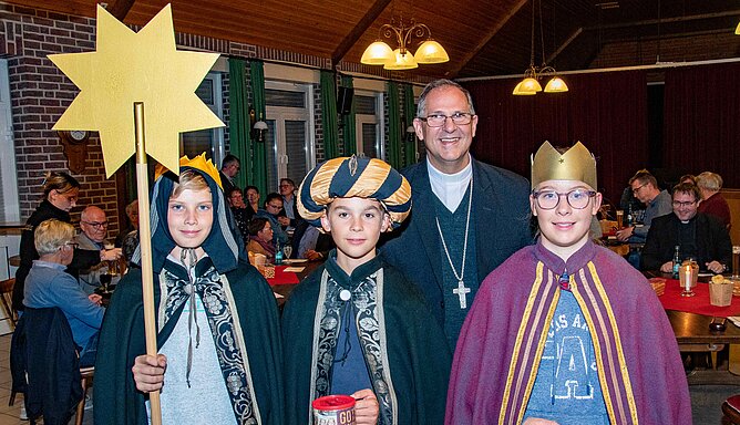 Drei als Sternsinger verkleidete Jugendliche stehen vor einem Mann.