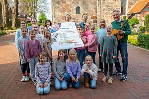 20 Mädchen und stehen vor einer Kirche und präsentieren ein Plakat des Chortages. Chorleiter Hans-Georg Schnabel hält eine Gitarre. 20 Mädchen und stehen vor einer Kirche und präsentieren ein Plakat des Chortages. Chorleiter Hans-Georg Schnabel hält eine Gitarre.