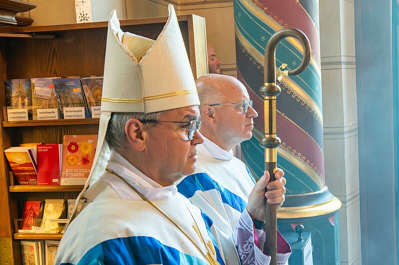 Ein Bischof und ein Priester stehen nebeneinander in einer kirche