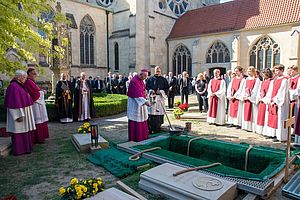 Vor einer offenen Grabstelle stehen Bischof Felix Genn und zahlreiche weitere Teilnehmende der Trauerfeier. 