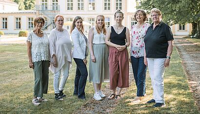 Sieben Frauen stehen auf einer Wiese vor einem großen Gebäude.