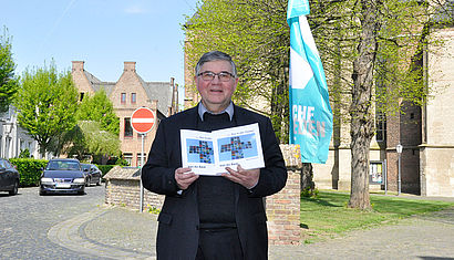 Pastor Alois van Doornick steht vor der St. Nicolai Kirche in Kalkar und hält zwei Ausgaben seines neuen Buches in den Händen.