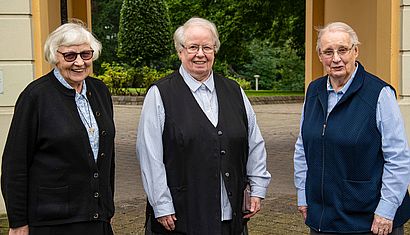 Drei Ordensschwestern stehen im Freien vor einem Torbogen.