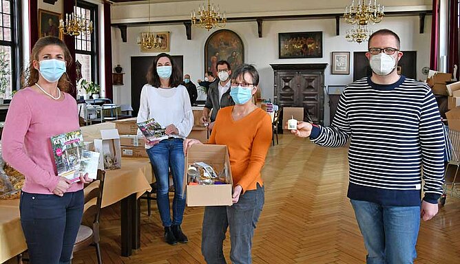 Mehrere Personen stehen in einem Saal und zeigen Andenken, die in ein Paket gefüllt werden.