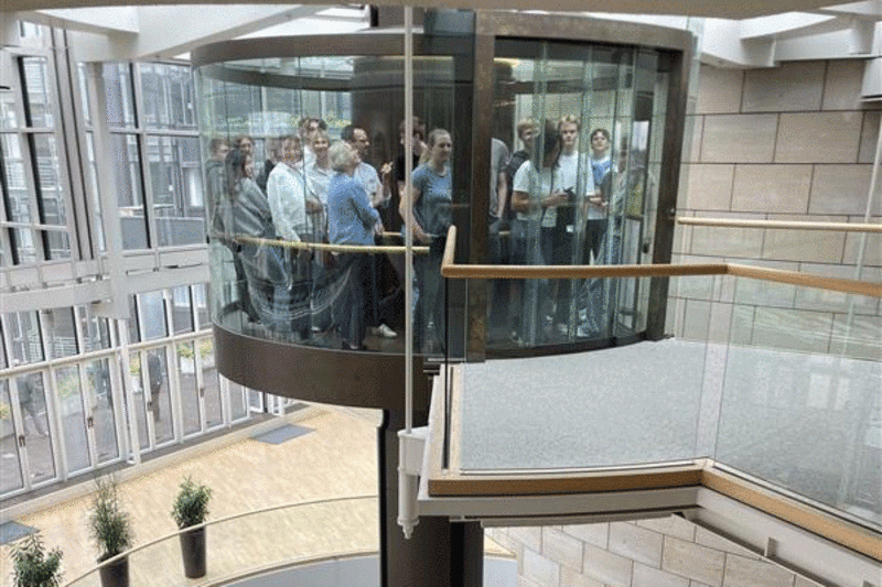 Eine Gruppe von Menschen fährt in einem gläsernen Aufzug.
