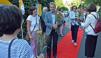 Hubert Lemken hat Blumen in der Hand und läuft über einen roten Teppich, an dem mehrere Frauen stehen.