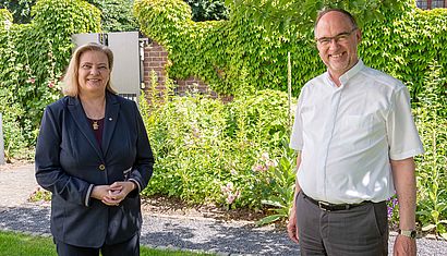 Sabine Weiss und Rolf Lohmann stehen mit Abstand nebeneinander in einem Garten im Schatten.