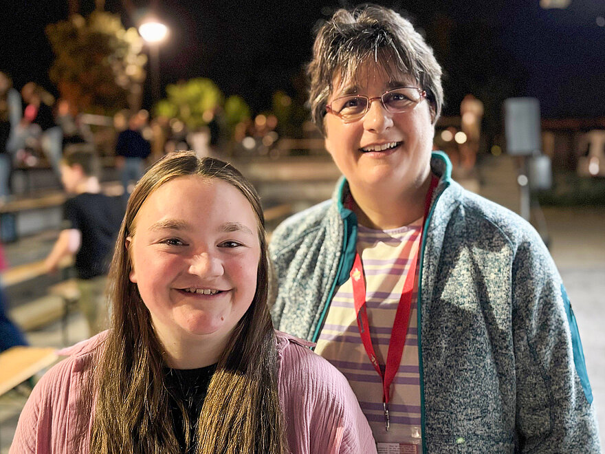 Links ist ein Mädchen im Teenageralter zu sehen. Rechts neben ihr, steht ihre Mutter. Beide lächeln in die Kamera. Links ist ein Mädchen im Teenageralter zu sehen. Rechts neben ihr, steht ihre Mutter. Beide lächeln in die Kamera.