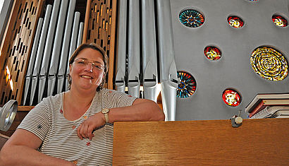 Annegret Walbröhl lehnt an der Orgel, hinter ihr sind die Orgelpfeifen und bunte Kirchenfenster zu sehen.