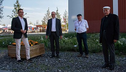 Vier Männer stehen mit Abstand nebeneinander auf dem Gelände der Landesgartenschau.