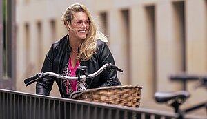 Sandra Reher steht steht lächelnd neben ihrem Fahrrad vor einem Verwaltungsgebäude. 
